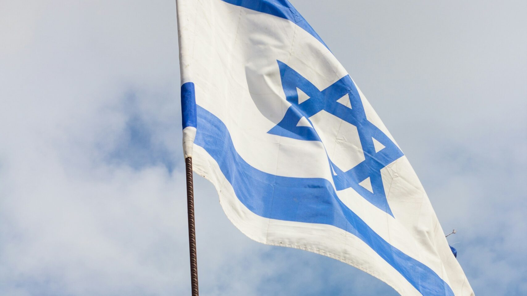 Die Flagge Israels. Zentral angeordneter blauer Davidstern zwischen zwei waagerechten blauen Streifen auf weißem Grund.